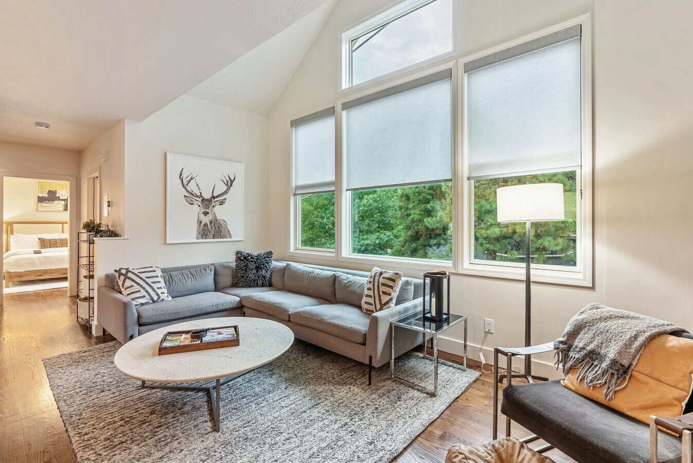A modern living room with a sectional sofa, a coffee table, and a large window with a view of greenery.
