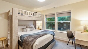 A bunk bed with a desk and chair, a window with a view of greenery, and a ceiling light.