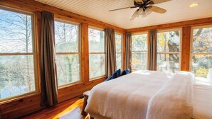 A bedroom with a large bed, wooden floors, and multiple windows with curtains. - Black Bear Lodge at gorgeous Lake Jocassee (Salem)
