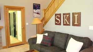 Ein Wohnzimmer mit einer Couch, Kissen, einer Lampe und einer Holztreppe.