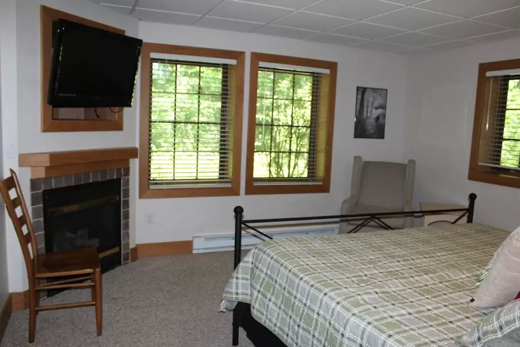 Ein Schlafzimmer mit Bett, Sessel, Kamin und Wandfernseher.