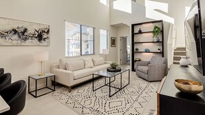 Ein modernes Wohnzimmer mit einer Couch, einem Couchtisch und Sesseln, einem Bücherregal und einem großen abstrakten Gemälde.