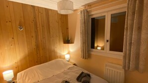 Une chambre avec un plafond en bois, un lit avec une literie blanche, une lampe de chevet, une fenêtre avec des rideaux et un radiateur.