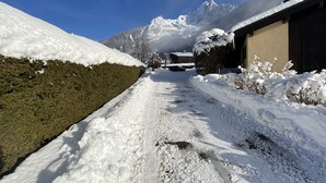 Un sentier enneigé menant à un bâtiment, avec une chaîne de montagnes en arrière-plan.