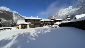 Un chalet à plusieurs étages, dont le toit est recouvert de neige, entouré de montagnes et surplombant un ciel dégagé.