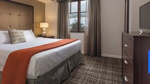 A hotel room with a large bed, two bedside tables, a TV, and a window with curtains.