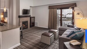 A modern living room with a fireplace, a kitchen area with a microwave, and a seating area with a sofa and ottomans.