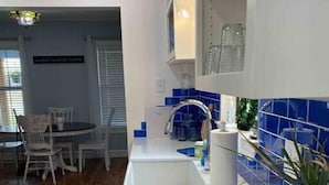 Une cuisine moderne avec un plan de travail blanc, un pare-feu bleu et un revêtement de sol en bois. On aperçoit à l’arrière-plan un coin repas avec une table et des chaises.