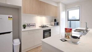 A modern kitchen with white cabinets, a microwave, a stove, and a sink. There's a sign that says "Home" and a box of Oats cereal on the counter.