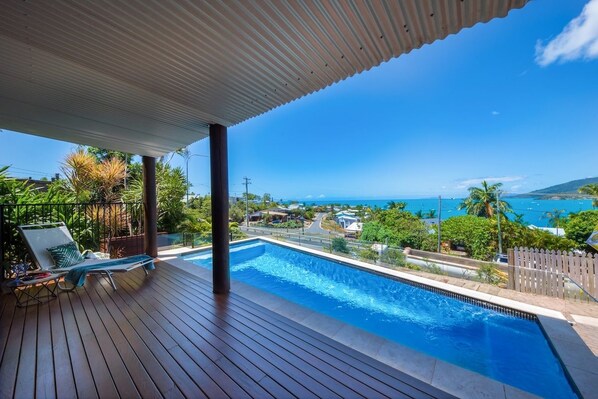 A wooden deck with a swimming pool, lounge chairs, and a view of the ocean. - 49 On Airlie - Airlie Beach (Airlie Beach)