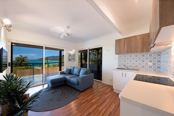Ein modernes Wohnzimmer mit einer großen L-förmigen Couch, einer Küchenzeile mit ornamentalem Rückspritzschutz und einem Balkon mit Meerblick.