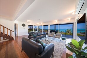 Ett rymligt vardagsrum med ett stort fönster med utsikt över havet, en trätrappa och en modern inredningsstil.