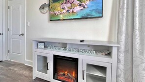 Ein Wohnzimmer mit Kamin, einem darüber befestigten Fernseher und einem Schild mit der Aufschrift 'Welcome to the Beach'.