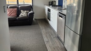 A compact kitchen with a refrigerator, stove, microwave, and sink. A leather couch is visible in the foreground, and a large window offers a view of a rural landscape. - TWIZEL - House near the lake (Twizel)