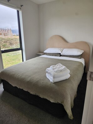 A neatly made bed with a beige headboard, a grey bedspread, and white pillows. A folded white towel is placed on the bed. - TWIZEL - House near the lake (Twizel)