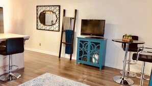 A modern living room with a wooden floor, a blue cabinet with a TV, a bar area, and a patterned rug. - Dreamy Summer Stay-Cozy Condo for Couples (St George)