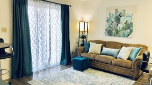 A living room with a brown sofa, blue cushions, a patterned rug, a dining area with a table and chairs, and a cactus painting on the wall. - Dreamy Summer Stay-Cozy Condo for Couples (St George)
