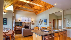 A spacious living area with a fireplace, wooden ceiling, and a kitchen island with a sink. - Rock Pond Condo 75 | Beautiful end unit at Saddleback (Sandy River Plantation)