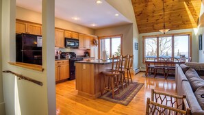 A spacious kitchen with wooden cabinets, a central island, and a dining area with a sofa and chairs. - Rock Pond Condo 75 | Beautiful end unit at Saddleback (Sandy River Plantation)