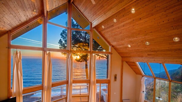 A room with large windows overlooking a body of water, wooden ceiling, and a view of the landscape. - Gorgeous Oceanview! by OceanviewHotTubs Tesla Charging Oceanfront! Shelter Cove (Whitethorn)