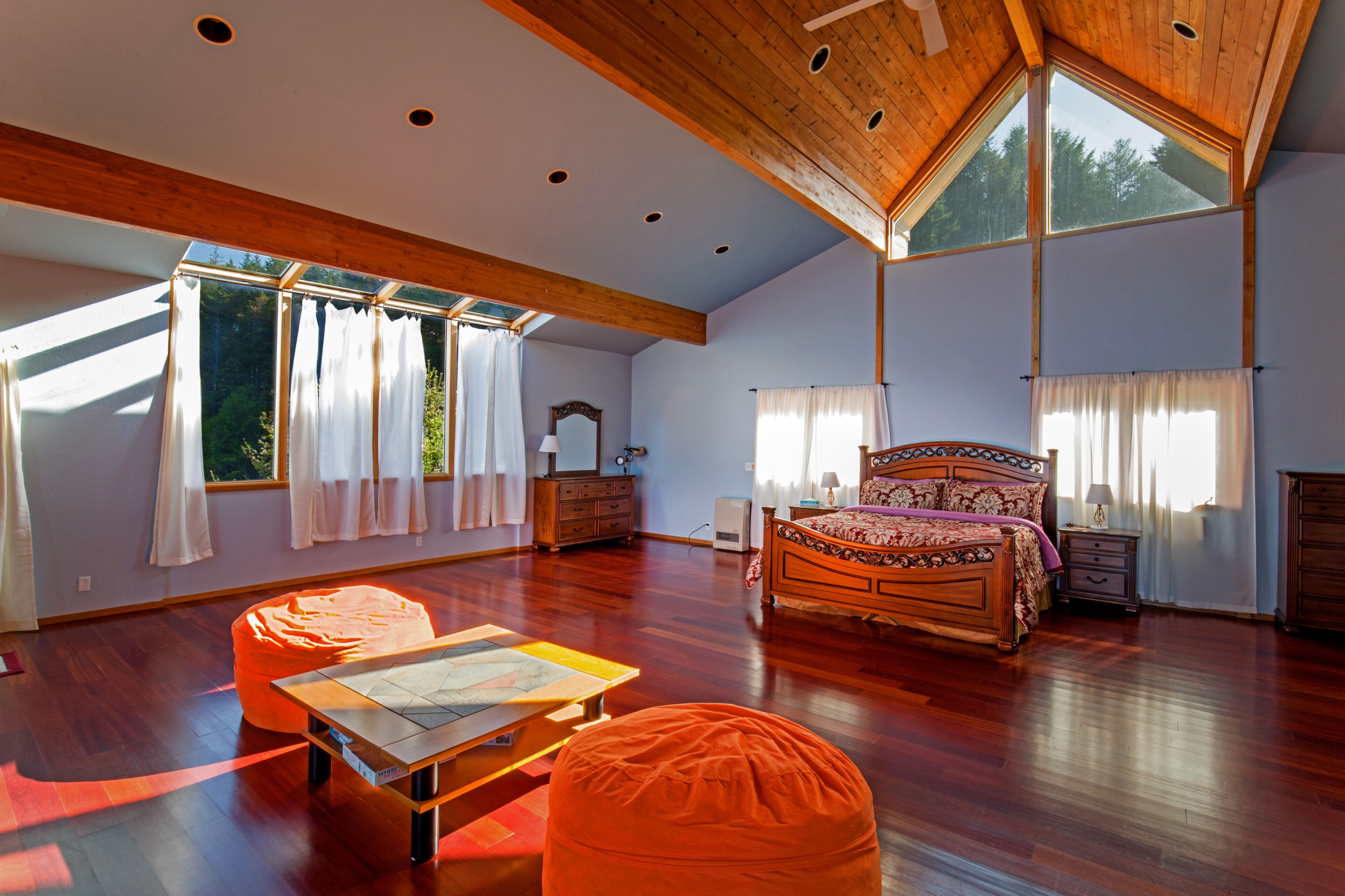 Une chambre spacieuse avec un grand lit, un plafond en bois et de grandes fenêtres.