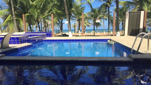 Piscina con azulejos azules, rodeada de palmeras y vista al océano.