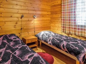 A wooden cabin room with two single beds, a nightstand, and a window with a checkered curtain. - Lapinkulta a by Interhome (Äkäslompolo)