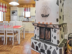 A cozy kitchen with a stone fireplace, wooden cabinets, and a dining area with chairs and a table. - Lapinkulta a by Interhome (Äkäslompolo)