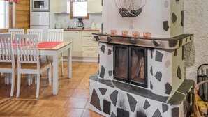 A cozy kitchen with a stone fireplace, wooden cabinets, and a dining area with white chairs and a red placemat. - Lapinkulta a by Interhome (Äkäslompolo)