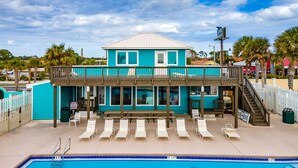 A turquoise two-story building with a pool area, including lounge chairs and a staircase leading to the upper level. - ❃ Walkable to Food & Fun ❃ Beach-Front Pool ❃ Canal-Side Home ❃ No Pet Fee (Panama City Beach)