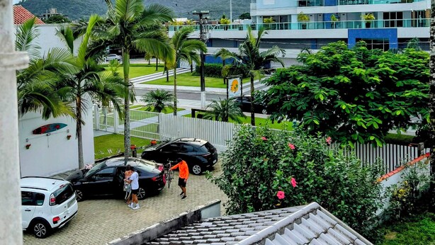 A modern building with multiple floors, a parking area with cars, and a view of a mountain in the background. - Triplex in Caiobá-Matinhos-Pr 200 m from the sea (Matinhos)
