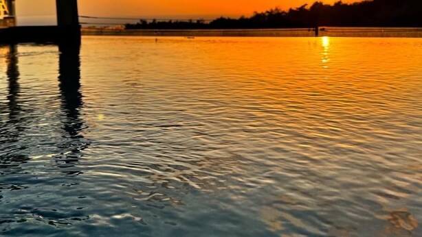 Atardecer sobre un cuerpo de agua tranquilo con una estructura a la izquierda.