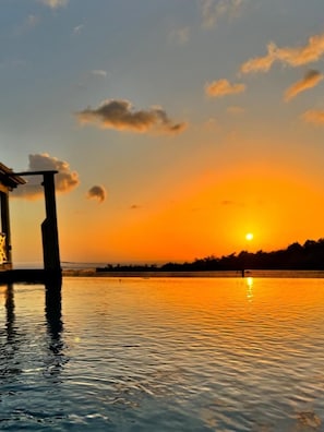 A sunset over a calm body of water with a structure on the left.