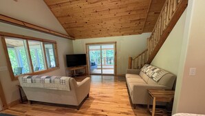 A spacious living room with wooden floors, a sofa, a television, and a staircase.