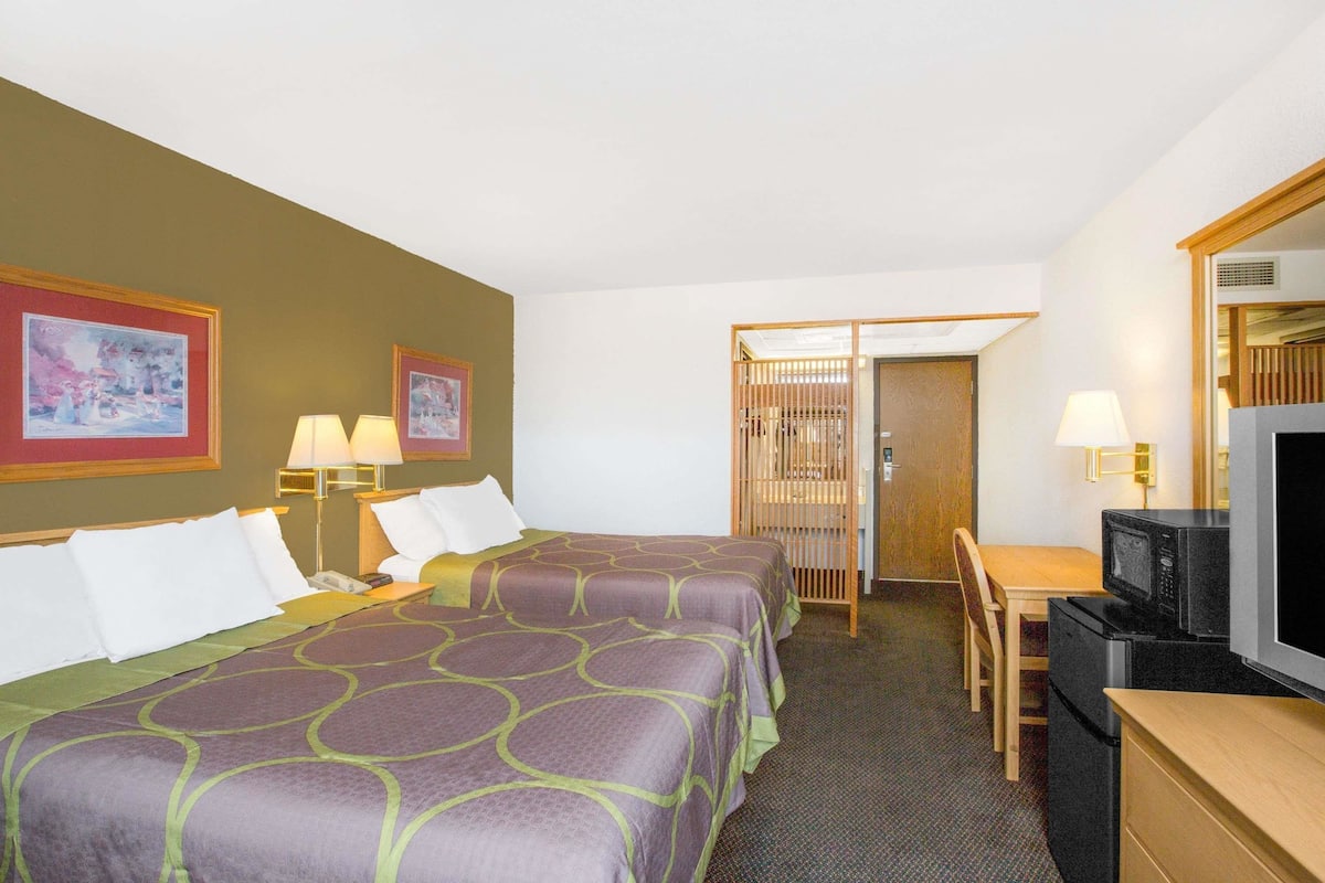 A hotel room with two beds, a desk with a chair, a television, and a door leading to a bathroom.