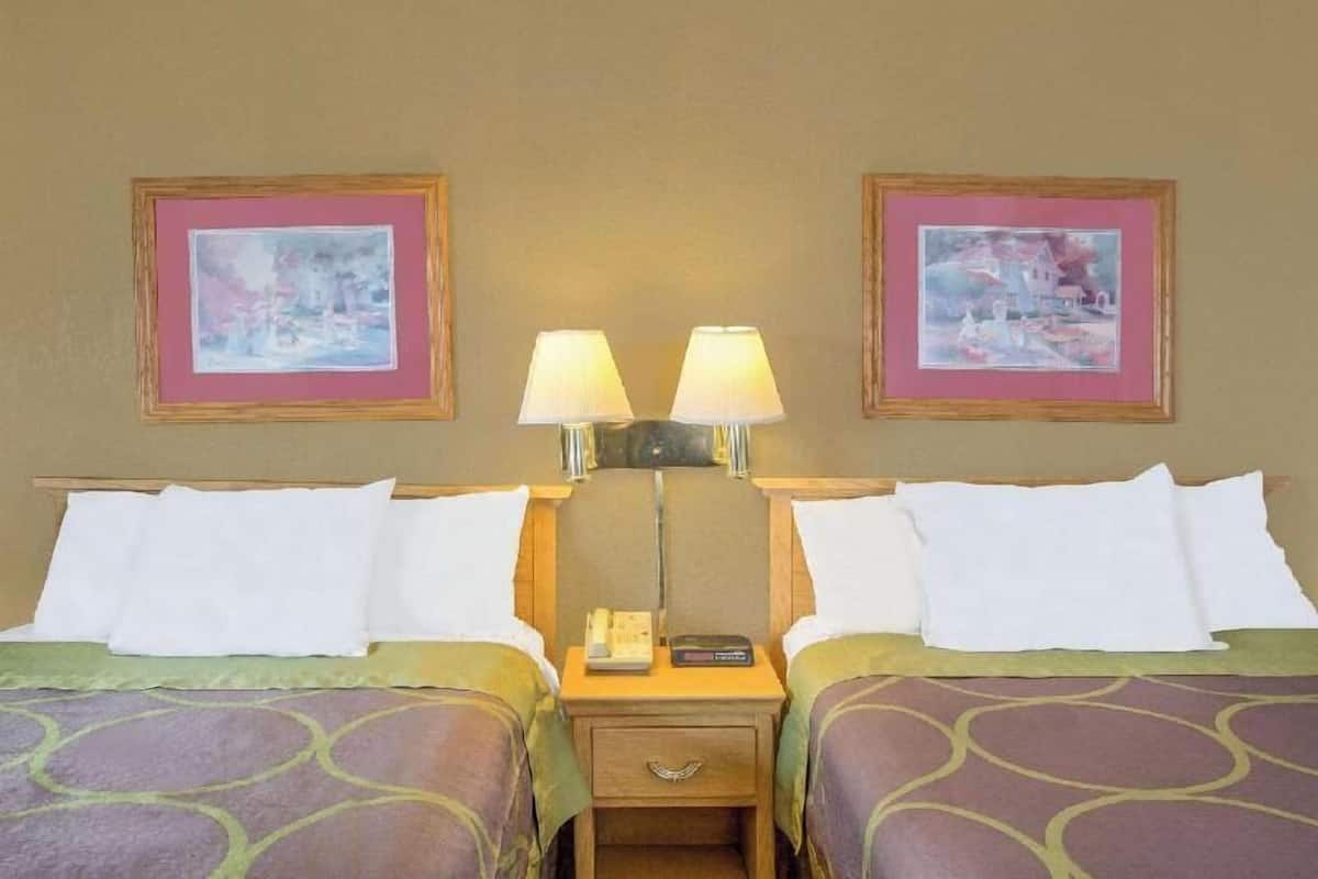 A hotel room with two beds, a nightstand with lamps, and framed artwork on the walls.