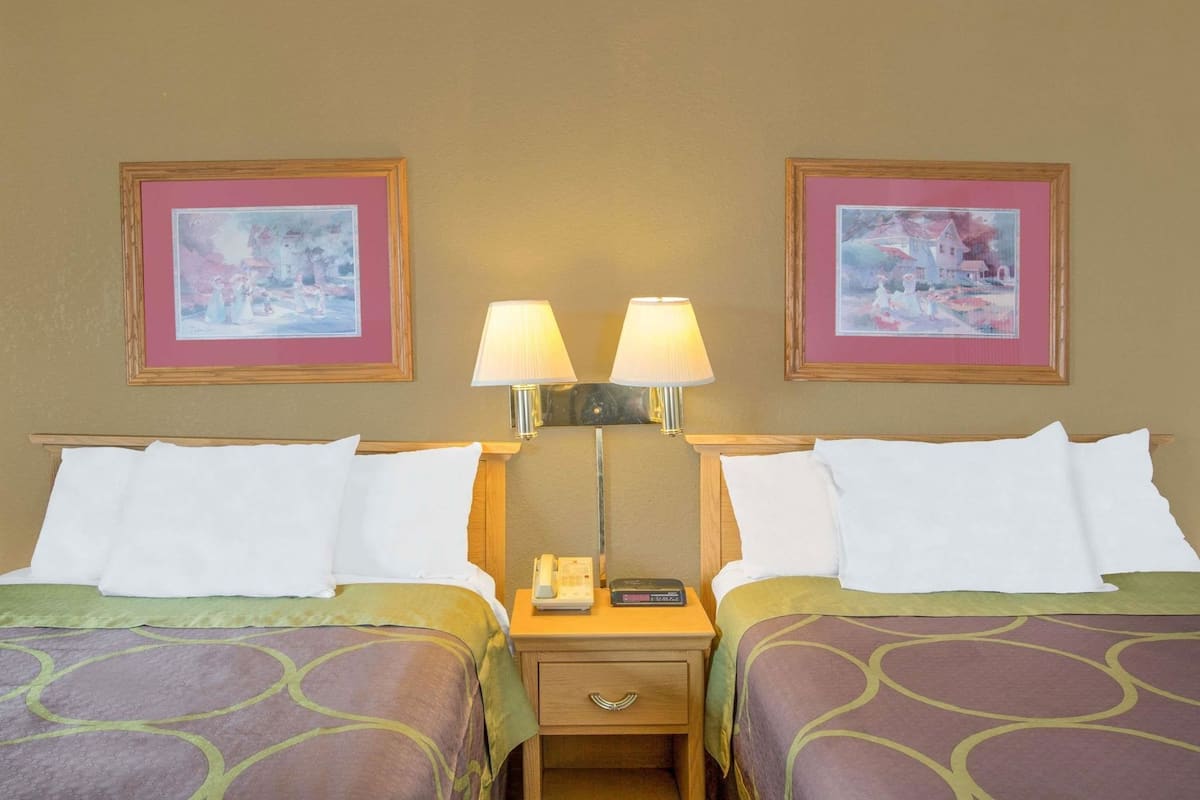 A hotel room with two beds, a nightstand with a lamp, a phone, and two framed pictures on the wall.