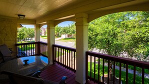 A covered porch with a glass table and chairs, a stone wall, and a view of a suburban street and greenery. - ★ Luxurious Two-Story Home ★ Near La Cantera/Rim (San Antonio)
