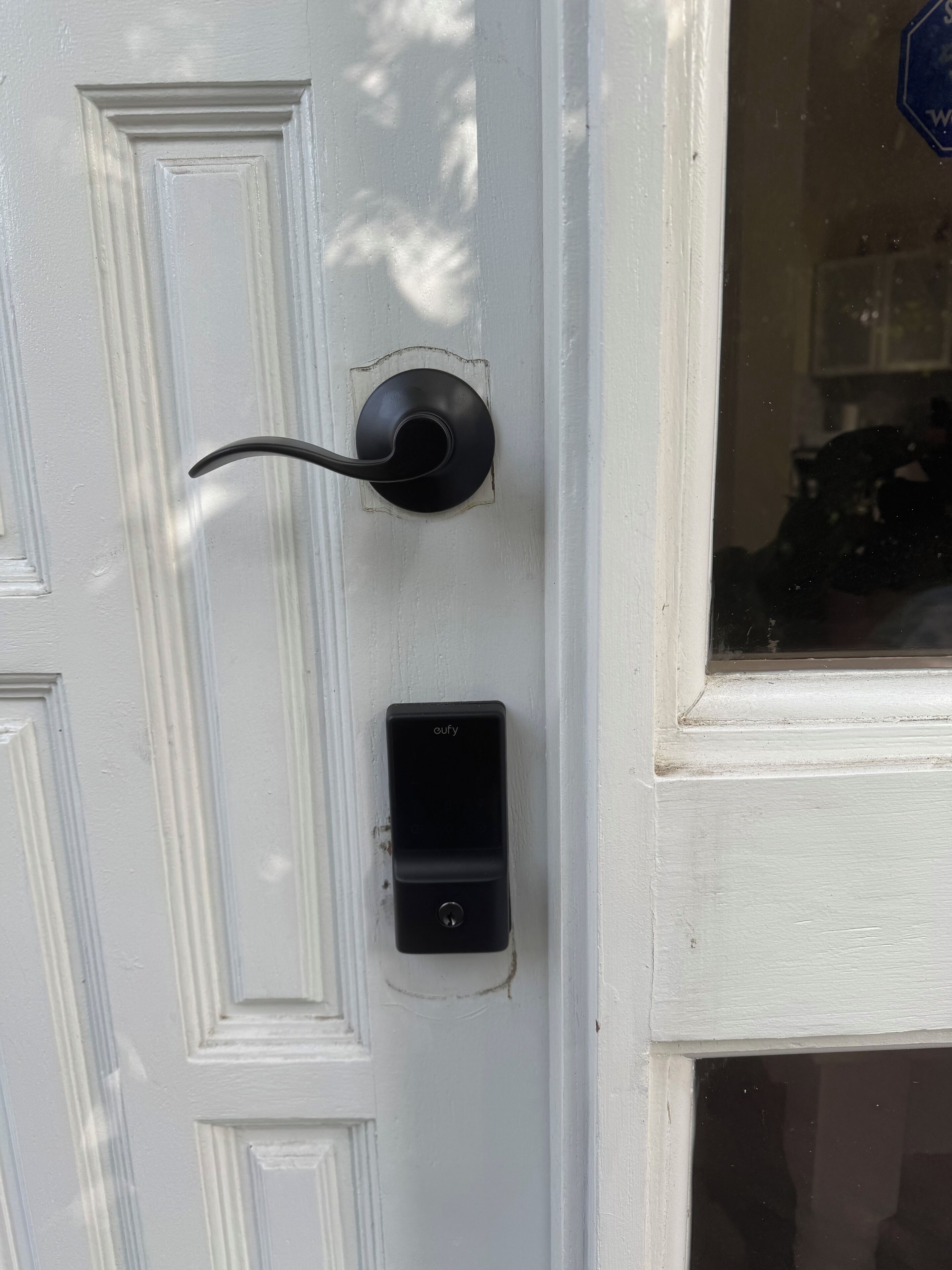 A white door with a black doorbell and a small black device mounted below it.