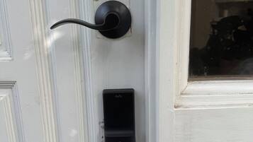 A white door with a black doorbell and a small black device mounted below it.