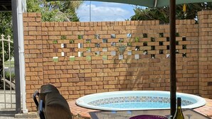 A glass table with a bottle of wine, a pool, and a brick wall with numbered tiles. - By The Harbour (Tauranga)