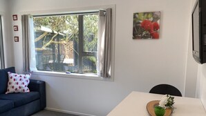 A room with a dark blue sofa, a white table with a wooden tray, and a window with curtains. - By The Harbour (Tauranga)