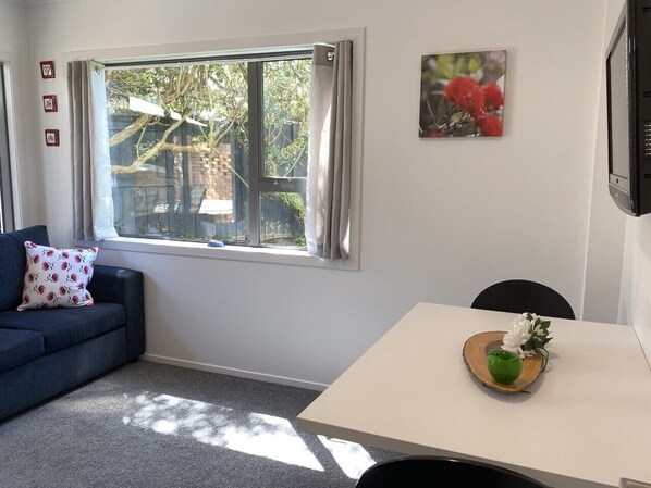 A room with a dark blue sofa, a white table with a wooden tray, and a window with curtains. - By The Harbour (Tauranga)
