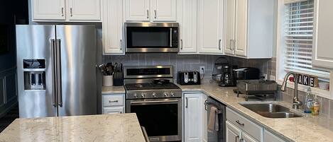 A modern kitchen with white cabinets, stainless steel appliances, and a marble countertop.