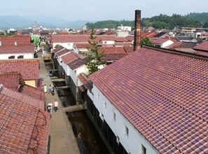 A narrow street lined with traditional buildings with red-tiled roofs, a narrow alley, and a distant view of mountains.