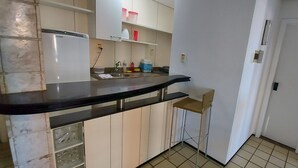 Een keuken met een zwart aanrecht, witte kasten, een klein krukje en een deur.