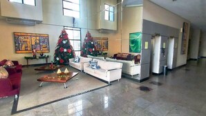 Een ruime lobby met een receptiebalie, twee witte banken, een rode fauteuil en twee kerstbomen.
