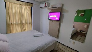 Een hotelkamer met een bed, een televisie waarop een bericht staat, een spiegel en een raam met gordijnen.