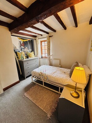Een slaapkamer met een bed, bedlampje, raam met gordijnen, radiator en een dressoir.