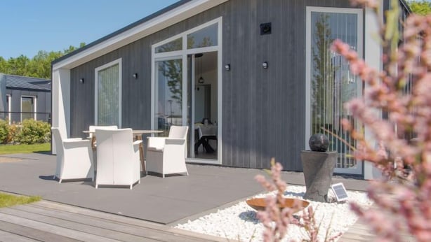 A modern house with a patio, white furniture, and a large window.